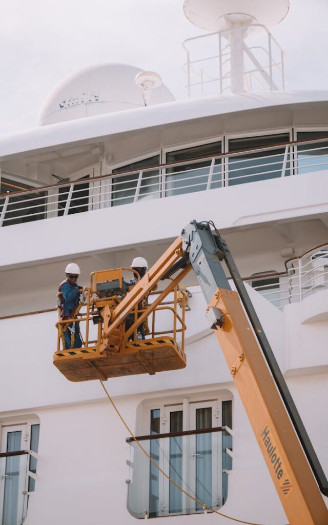 Two workers on a scissor lift performing maintenance on a cruise ship in Málaga, Spain.